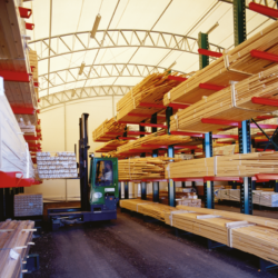 Insida av industrihall inom träindustri. Lagerhyllor med virke syns i bild.
