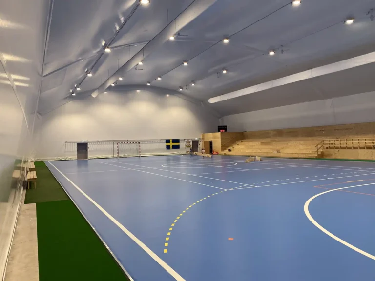 Idrottshallen Gullspång Arena invändigt. En isolerad tälthall för utövning av idrottsaktiviteter. Med blått golv och träläktare